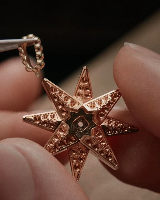 Close-up of a person holding a rose-gold star-shaped pendant with intricate geometric patterns and a small gold ring attachment.