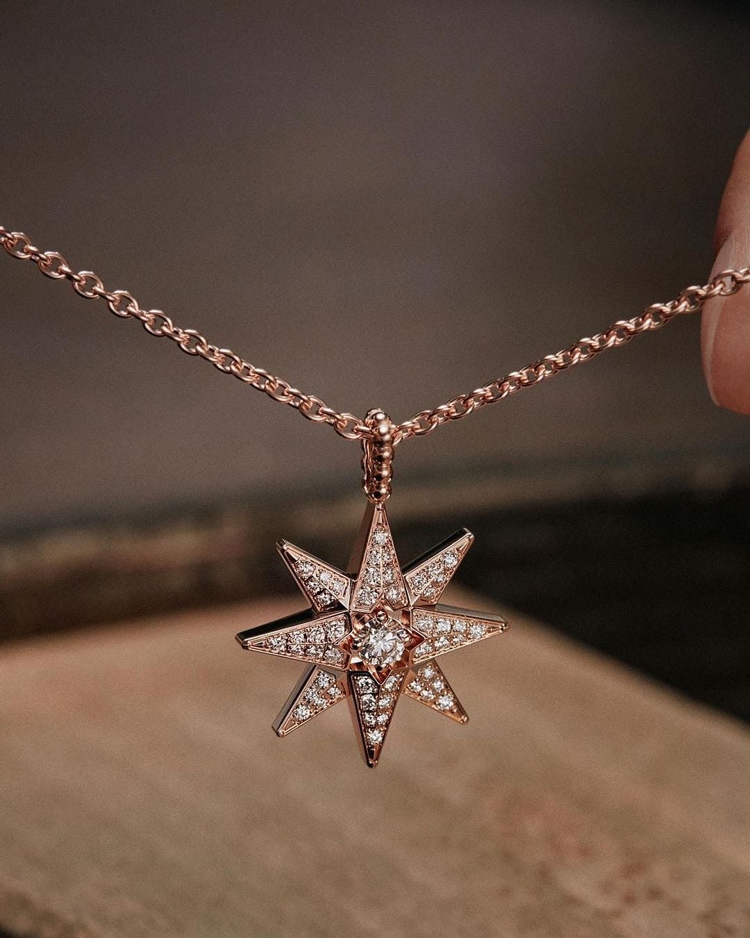 Elegant star pendant necklace made of rose gold with sparkling gem detailing on a matching delicate chain, against a soft brown backdrop.