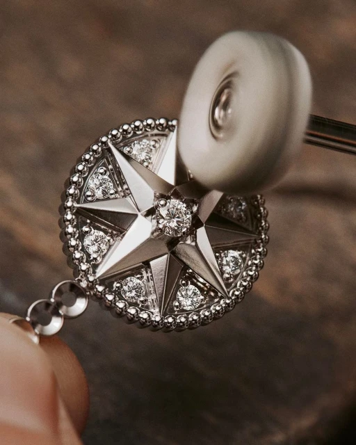 Close-up of a round metal pendant with star design and diamonds being polished with a white buffing wheel on a jewelry tool.