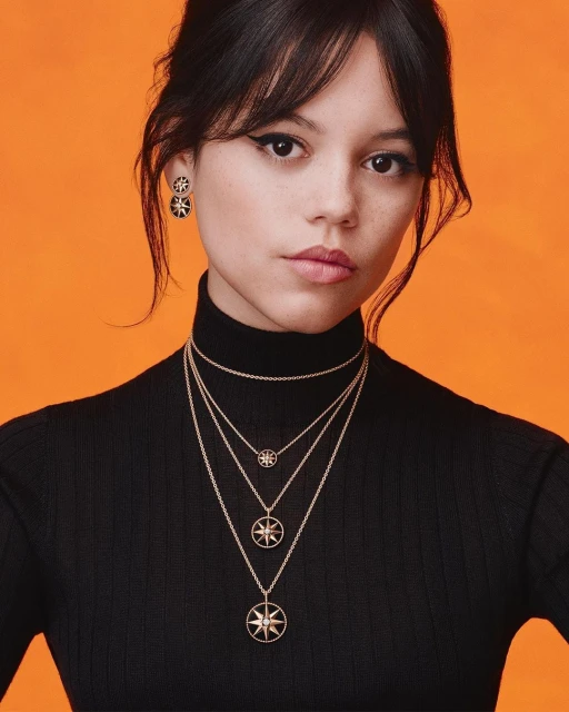 Headshot of brunette woman wearing a black turtleneck and layered necklaces with starburst pendants against an orange background.