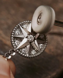 Close-up of a circular diamond pendant being polished with a rotating wheel on a workshop surface.