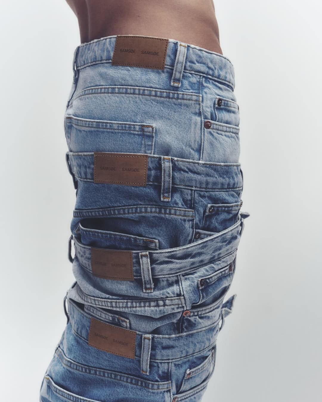 A stack of folded denim jeans with brown leather brand labels, presented on a clean white background, showcasing a fashion editorial style.