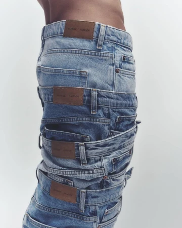 A stack of folded denim jeans with brown leather brand labels, presented on a clean white background, showcasing a fashion editorial style.