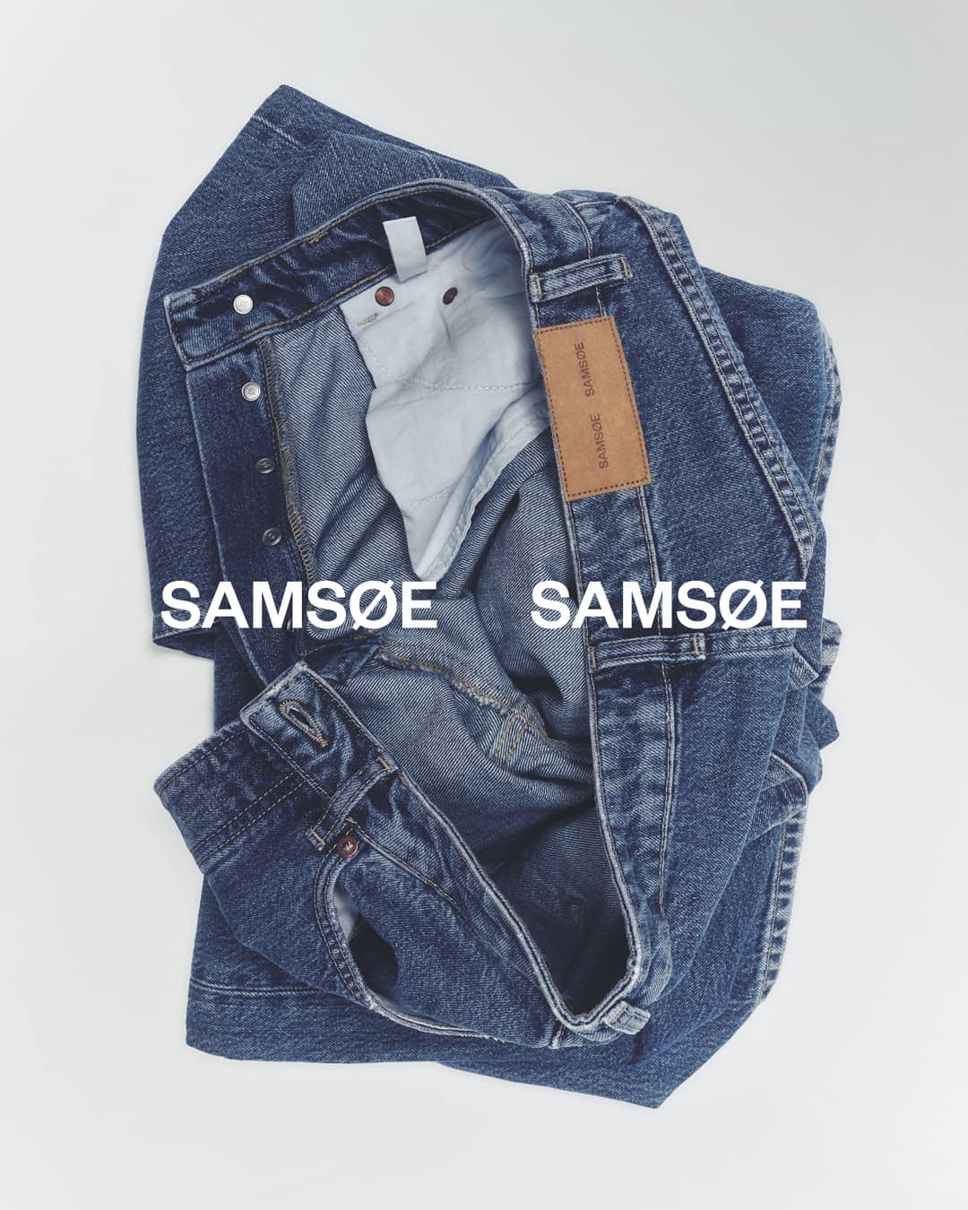 Folded blue denim jeans by Samsøe Samsøe on a white backdrop, showcasing the brand's label and design details in a studio product shot.
