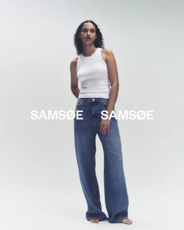 Fashion model poses in a white tank top and wide-leg blue jeans against a neutral backdrop, showcasing contemporary casual style.