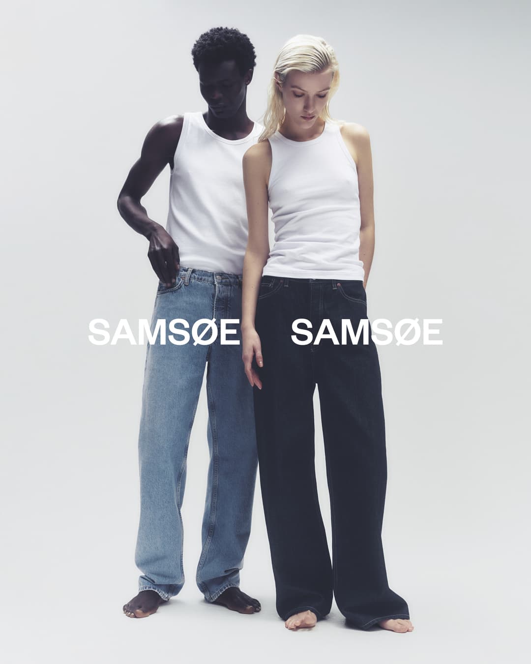 Fashion campaign shot of a Black male and white female standing side-by-side wearing casual tops and jeans against a clean background.