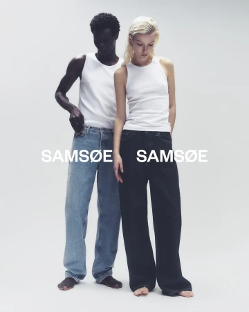 Fashion campaign shot of a Black male and white female standing side-by-side wearing casual tops and jeans against a clean background.