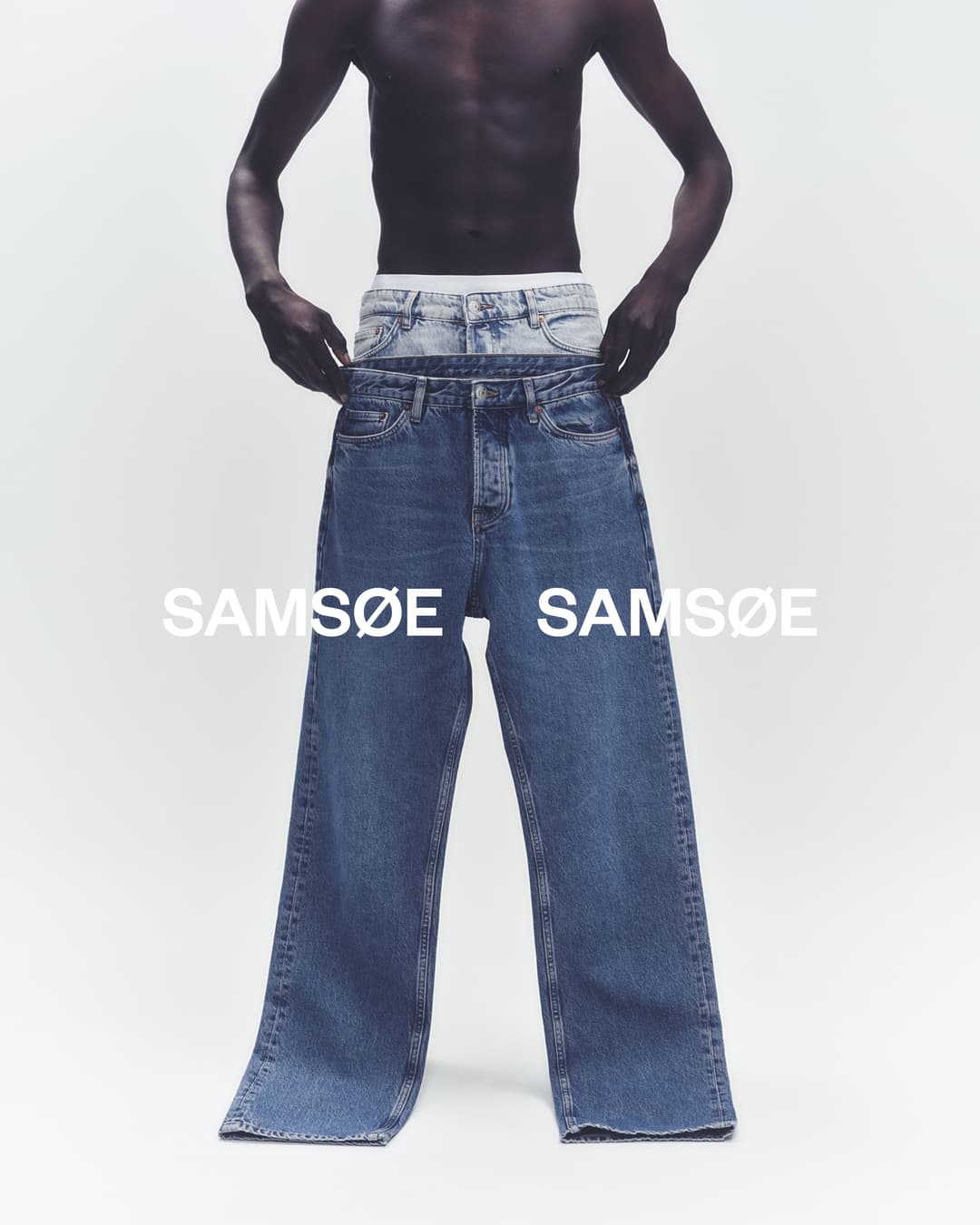 Dark-skinned male torso modeling two pairs of blue jeans in a bright photo studio; Samsøe Samsøe brand text visible.