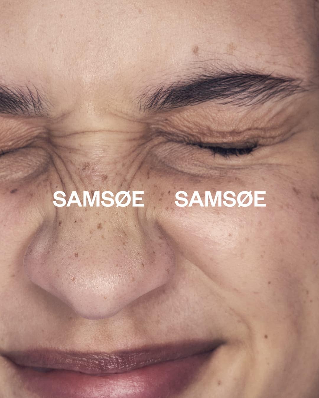 Close-up of an adult female's face with a wrinkled brow, freckles, and eyes mostly closed, with the brand name SAMSOE repeated twice.
