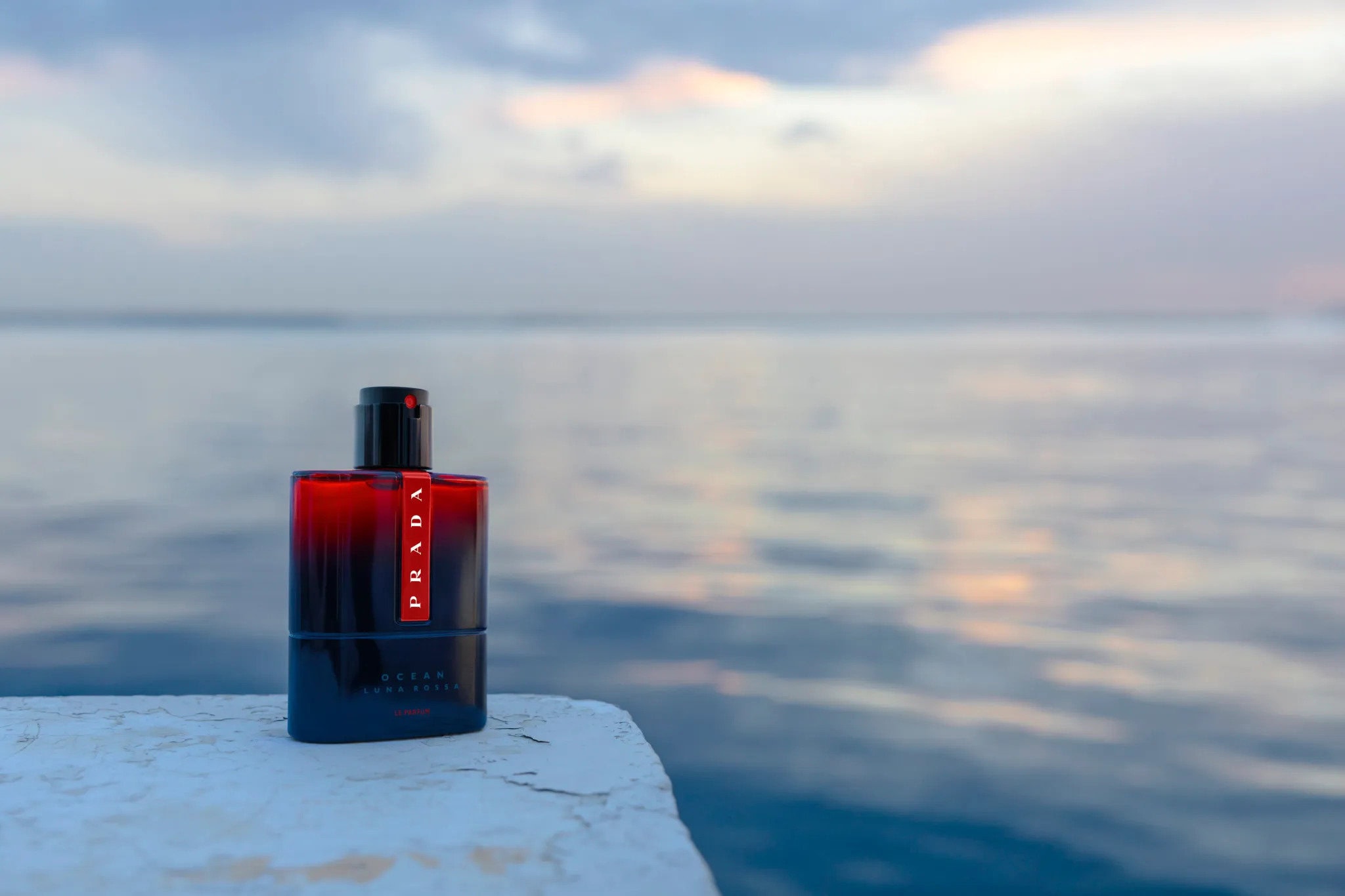 Prada Ocean fragrance bottle in a product shot. Red and black colorway with ocean background. Beauty and fashion industry content.