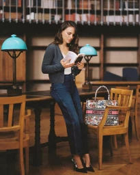 Natalie Portman leaning against a library table reading a book, next to a Dior tote bag on a chair.