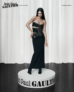 Model standing on a branded round white platform wearing a black leather strapless bodice and a long black skirt