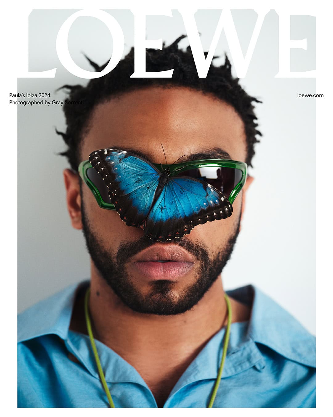 Magazine cover featuring a man with a butterfly on his face wearing green glasses and a blue button-down shirt against a white background.