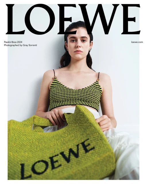 Loewe fashion advertisement featuring a woman with a green knit top and bag, posing indoors against a white background with bold text.