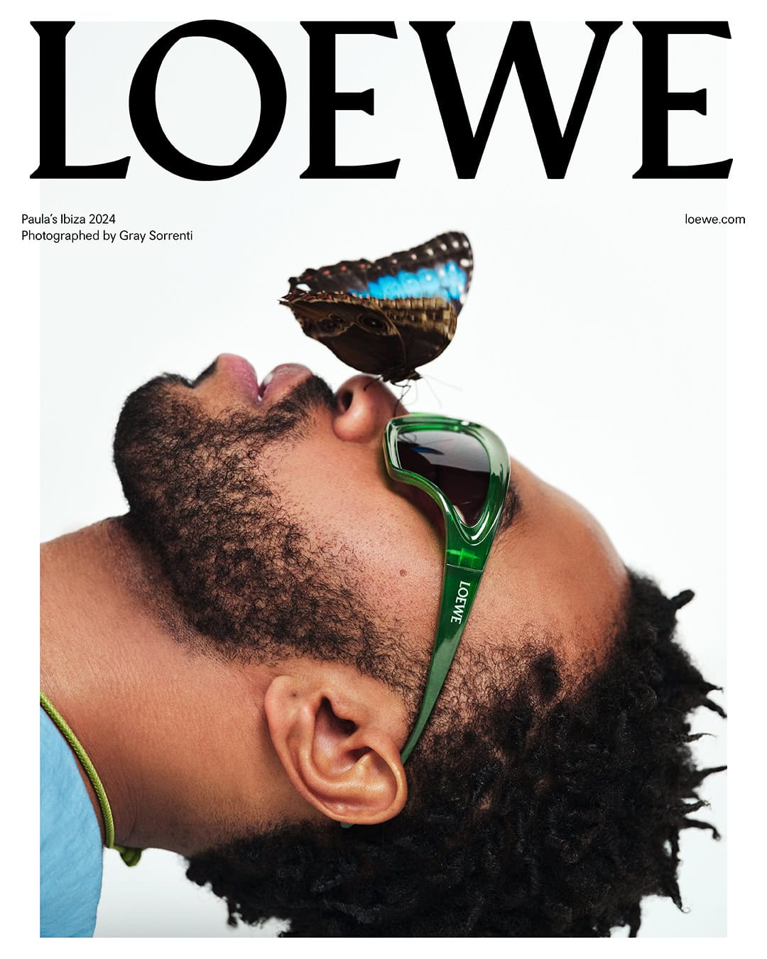 Loewe campaign image featuring an adult man with a butterfly on his nose, wearing green sunglasses against a white backdrop.