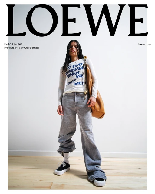 Fashion shot featuring a young woman in baggy jeans and a long-sleeve shirt, posing with a tan leather bag against a white backdrop.