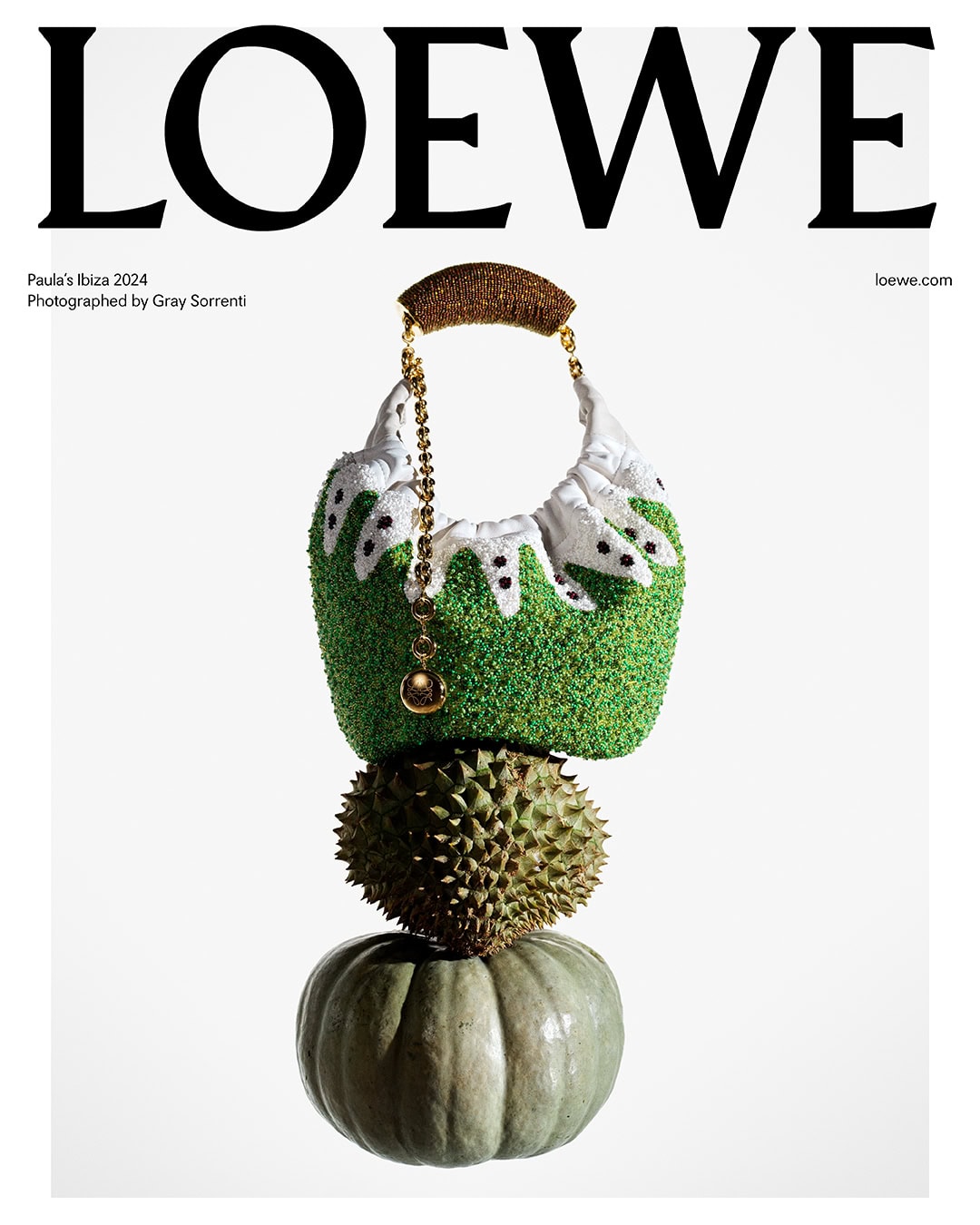 Loewe handbag with textured green and white design, durian, and pumpkin stacked on a white background, studio lighting for fashion editorial.