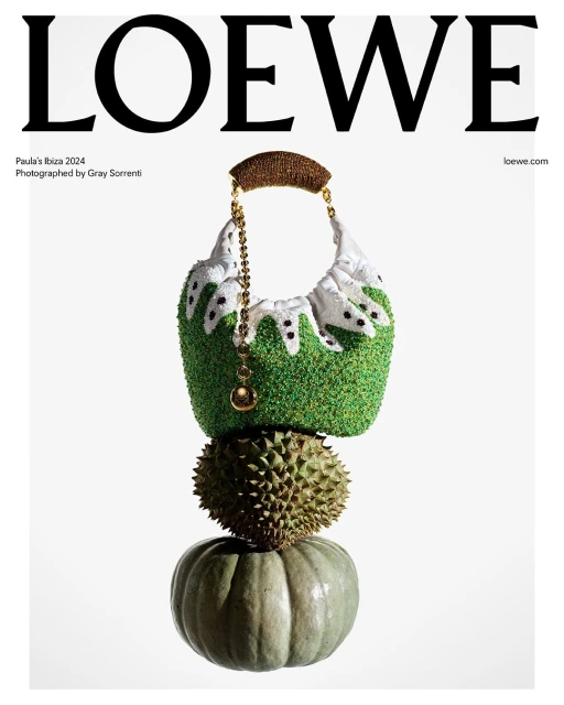 Loewe handbag with textured green and white design, durian, and pumpkin stacked on a white background, studio lighting for fashion editorial.