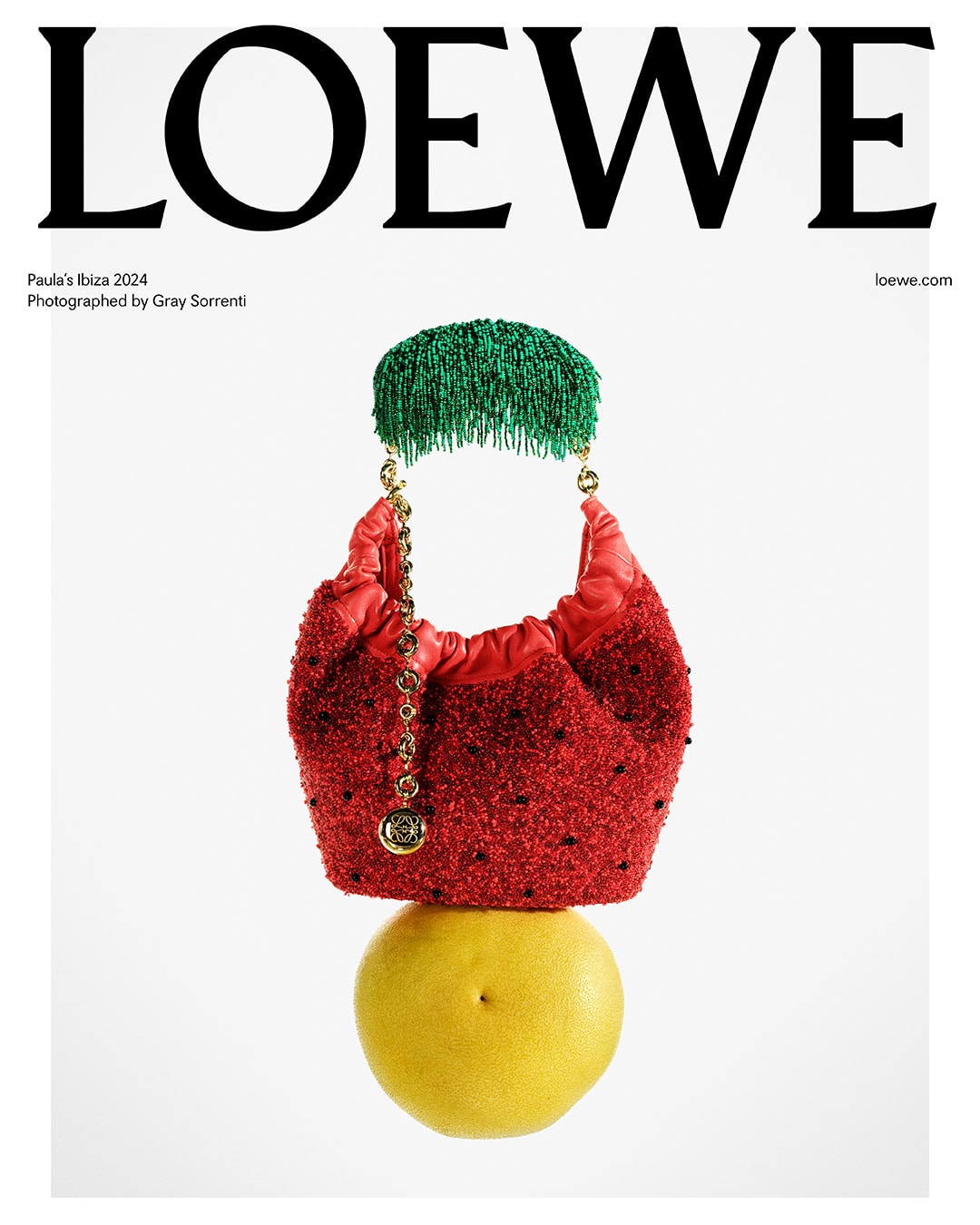 Loewe editorial fashion still life: red beaded handbag on top of yellow citrus fruit, adorned with green beaded fringe accessory.