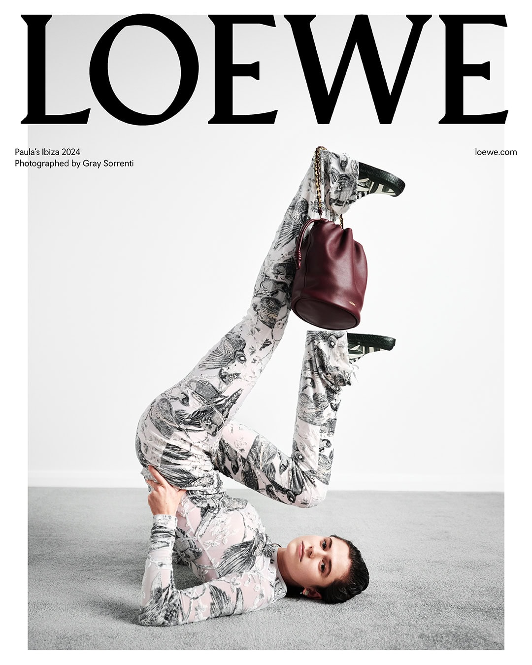 Loewe Paula's Ibiza 2024 campaign image features a model in a printed catsuit doing a handstand with a leather bucket bag.