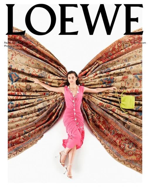 Fashion editorial shot: woman in pink dress lying amid antique rug and holding lime green handbag with a white backdrop.