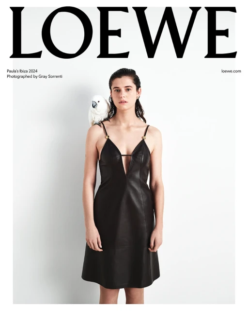 Fashion editorial featuring a woman in a black dress with a white cockatoo perched on her shoulder against a white background.