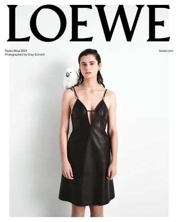 Fashion editorial featuring a woman in a black dress with a white cockatoo perched on her shoulder against a white background.