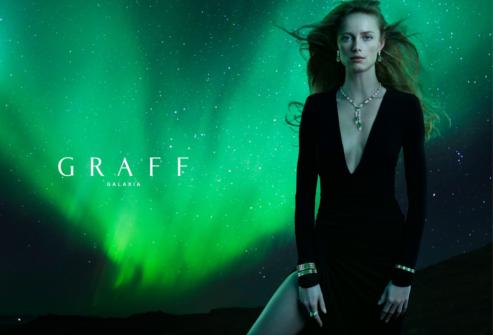 Elegant woman in black dress and jewellery poses against a green aurora borealis backdrop for a Graff Galaxia jewellery advertisement.
