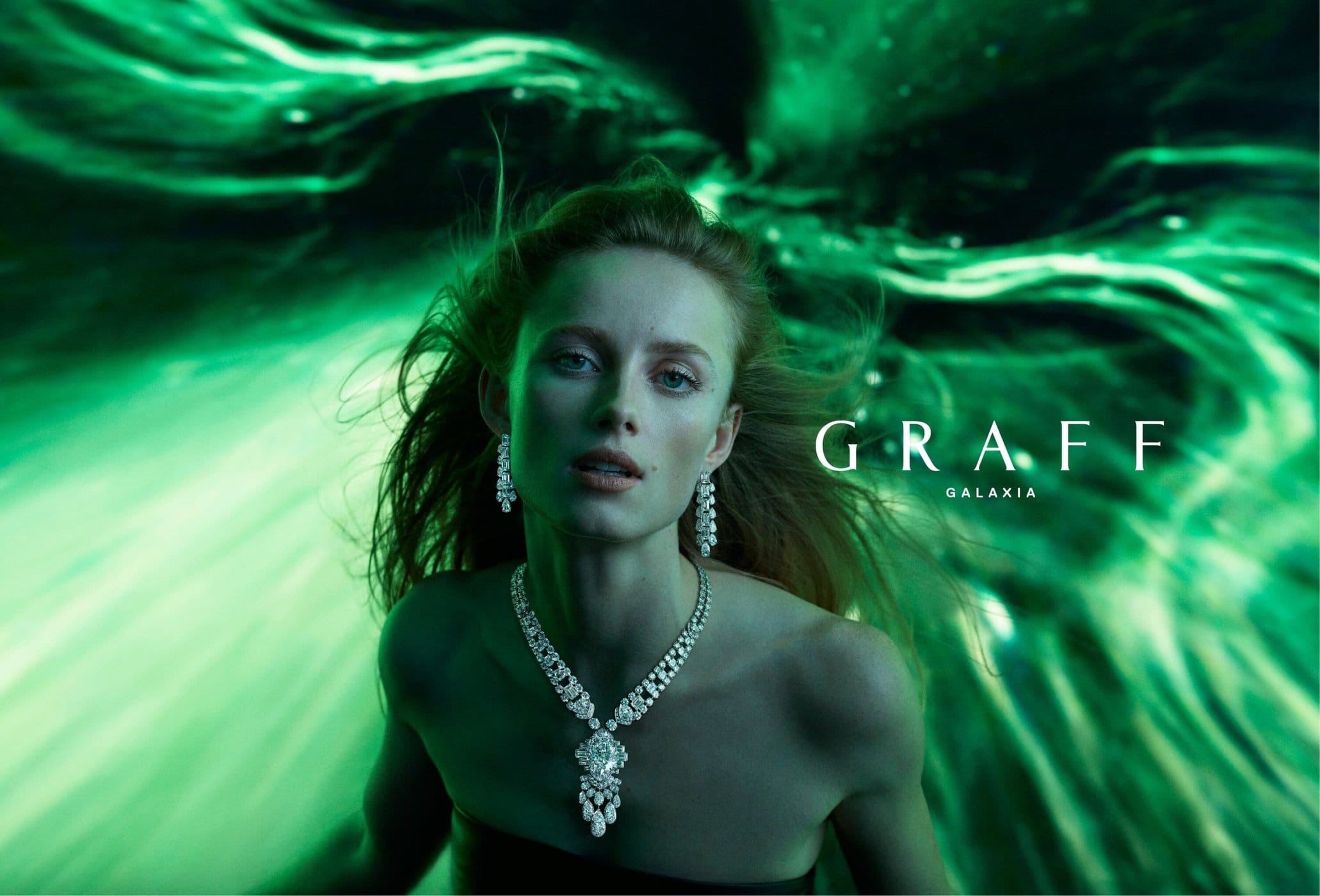 Woman wearing Graff Galaxia jewelry against a green abstract background. The long necklace, earrings, and overall presentation highlight high fashion.