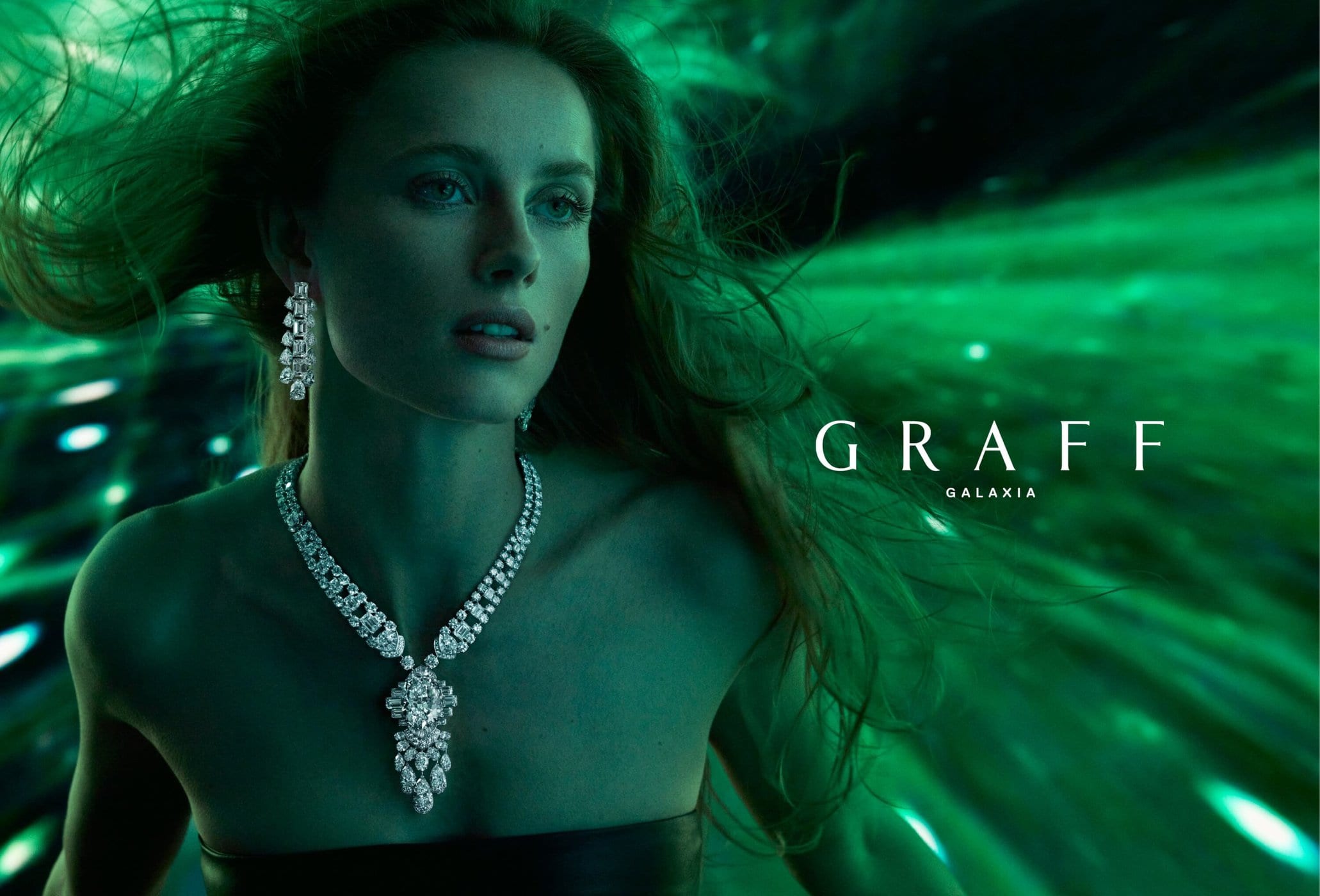 Elegant woman in emerald light showcases a Graff Galaxia diamond necklace and earrings, captured in a glamorous beauty shot. Jewelry focus.