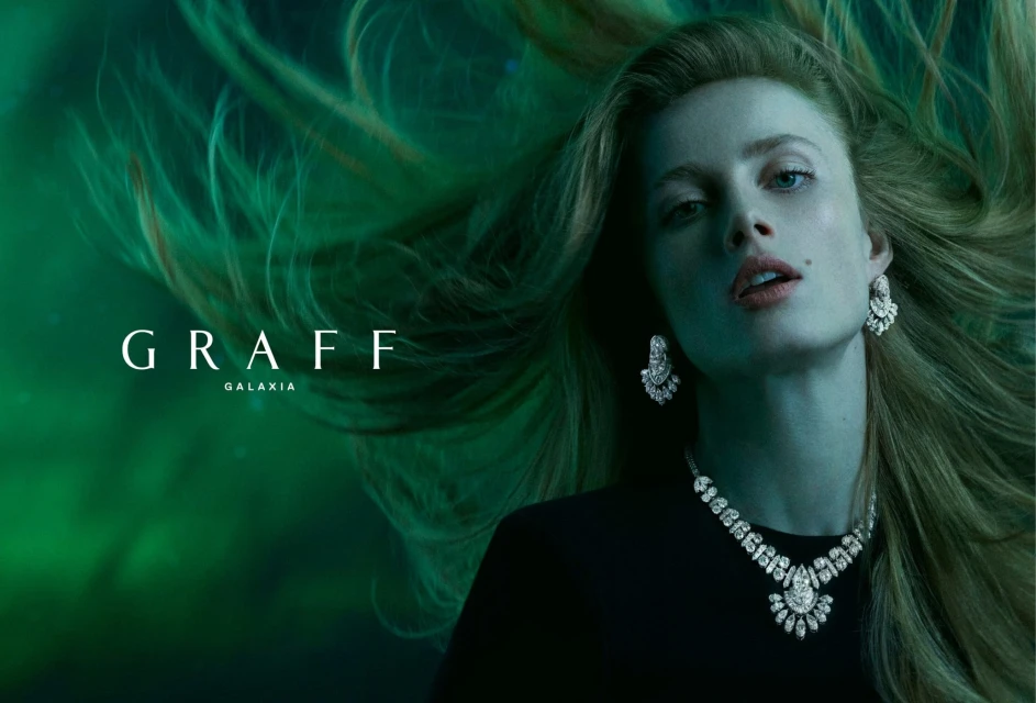 Blonde woman with statement diamond jewelry poses in front of a green background for GRAFF Galaxia jewelry advertisement.