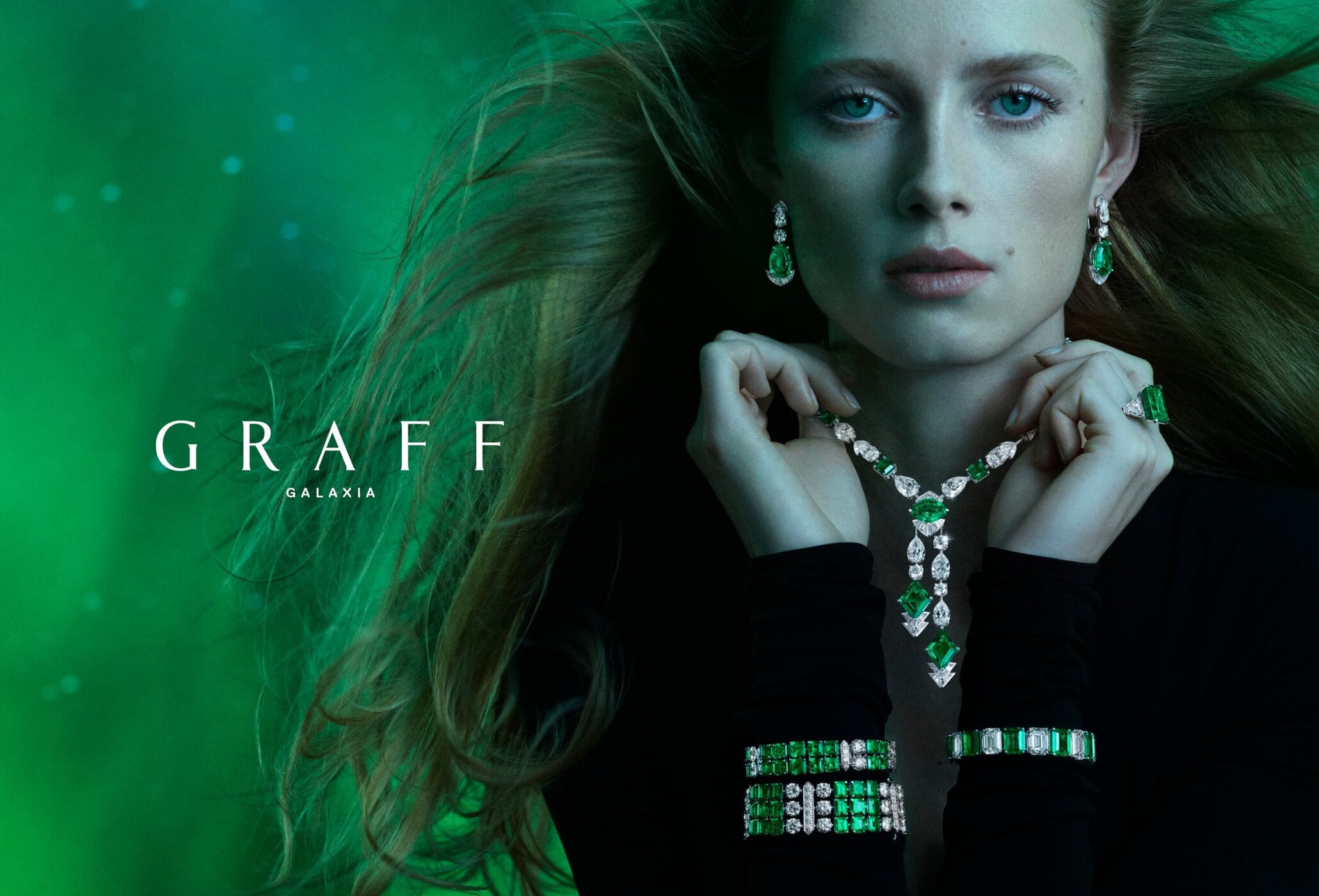 A woman with long brown hair poses wearing green and white jewelry, including a necklace, earrings, bracelets, and a ring, on a green background.