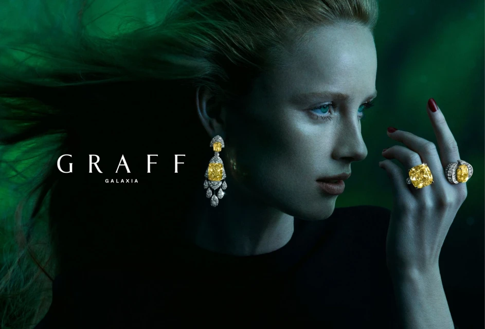 Blonde woman with yellow diamond earrings and rings in a jewellery advertisement, highlighted against a dark green background.