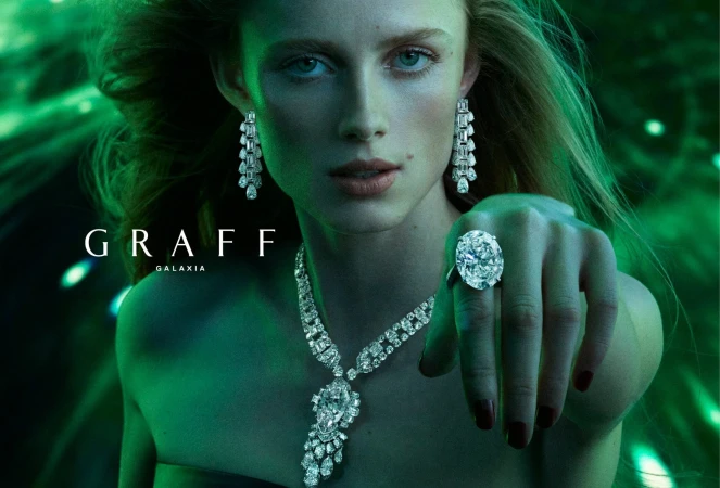 A woman is showcasing sparkling Graff jewelry, including a ring, earrings, and necklace, against a green background in a close-up shot.