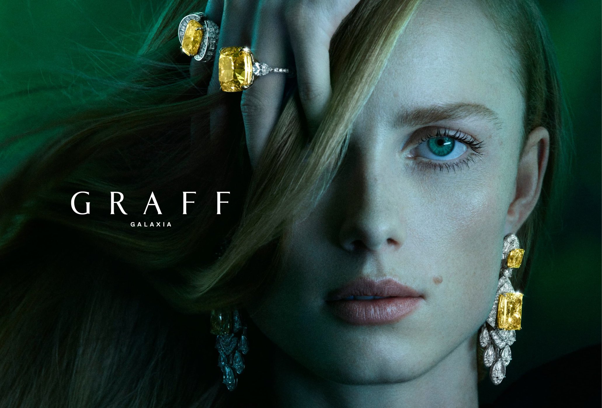 Close-up of a fair-skinned woman wearing yellow diamond jewelry by Graff Galaxia against a dark green background in a portrait orientation.