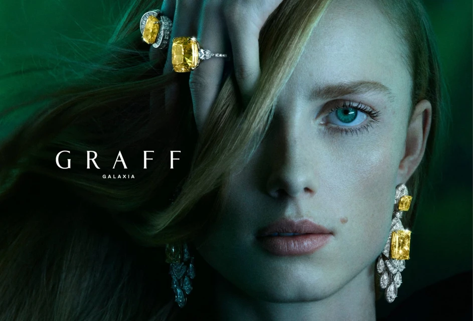 Close-up of a fair-skinned woman wearing yellow diamond jewelry by Graff Galaxia against a dark green background in a portrait orientation.