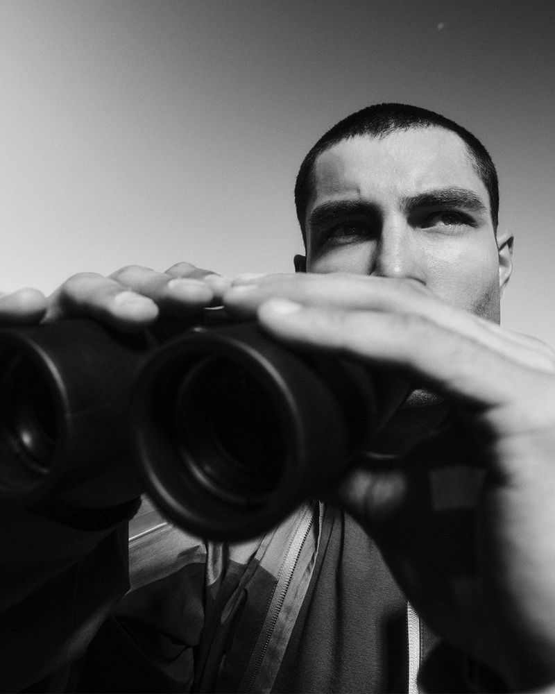 A man gazes through binoculars in a black and white photo, capturing a close-up view of his face and the optical device.