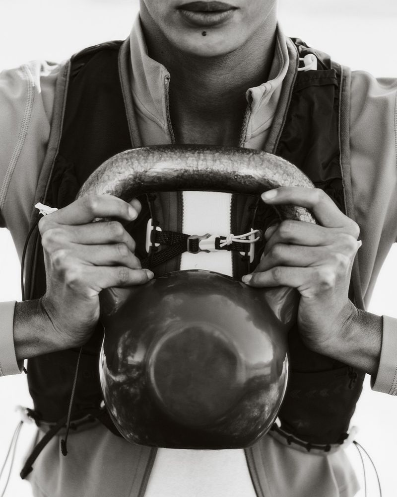 Black and white portrait of a person holding a kettlebell, focusing on the hands, fitness equipment, and upper body workout.
