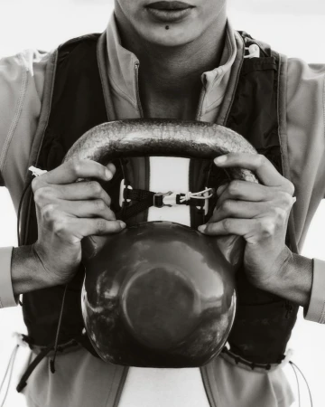 Black and white portrait of a person holding a kettlebell, focusing on the hands, fitness equipment, and upper body workout.