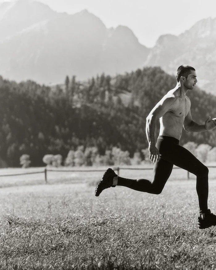Shirtless man running across a field with distant mountains under an overcast sky for Land Rover Defender Wyoming 2025.