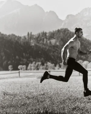 Shirtless man running across a field with distant mountains under an overcast sky for Land Rover Defender Wyoming 2025.