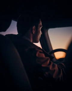 Man driving a vehicle during sunset viewed from inside the cabin silhouette style