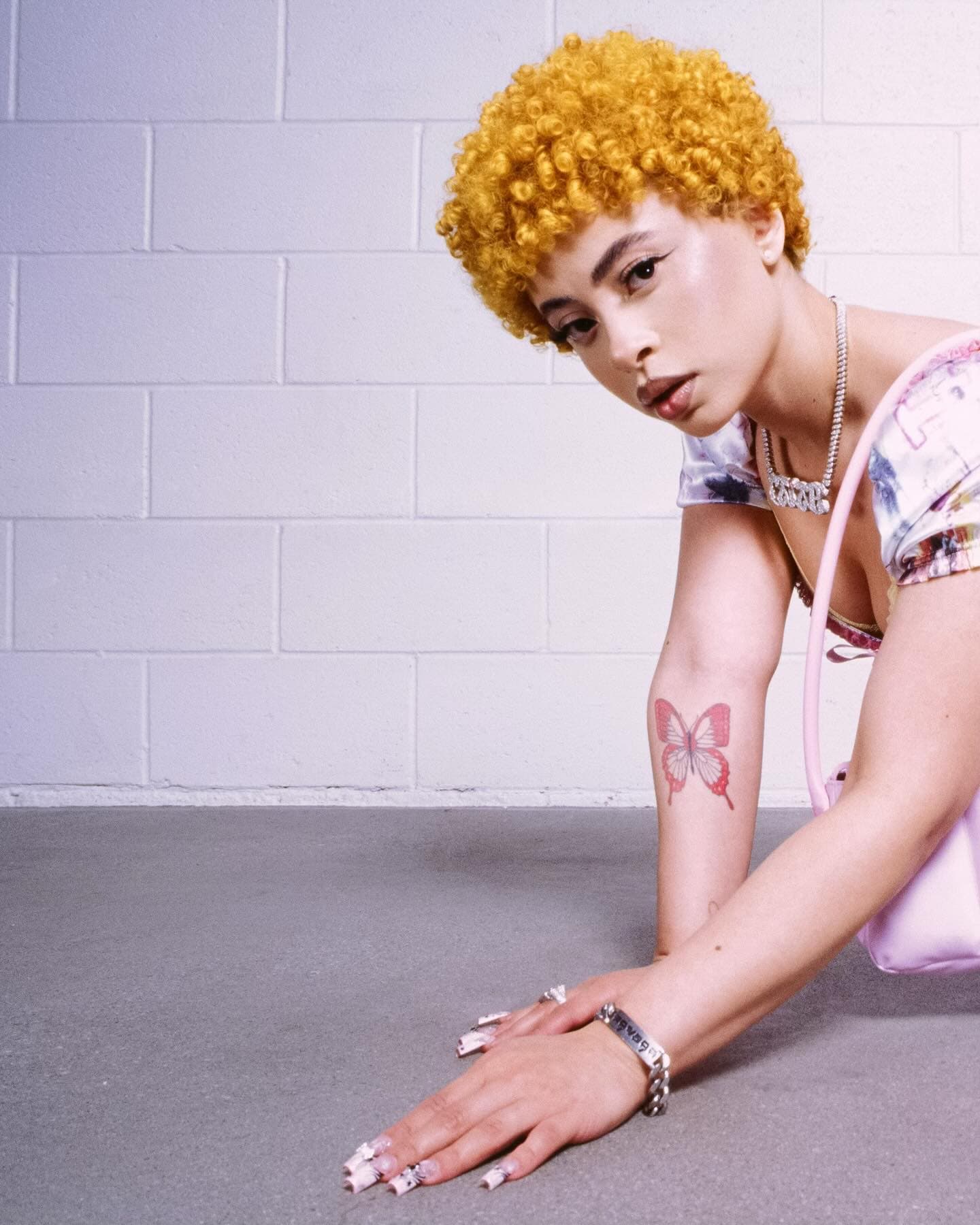 Woman with short golden hair and butterfly tattoo poses indoors.  Close-up fashion portrait, wearing silver jewelry and colorful top.
