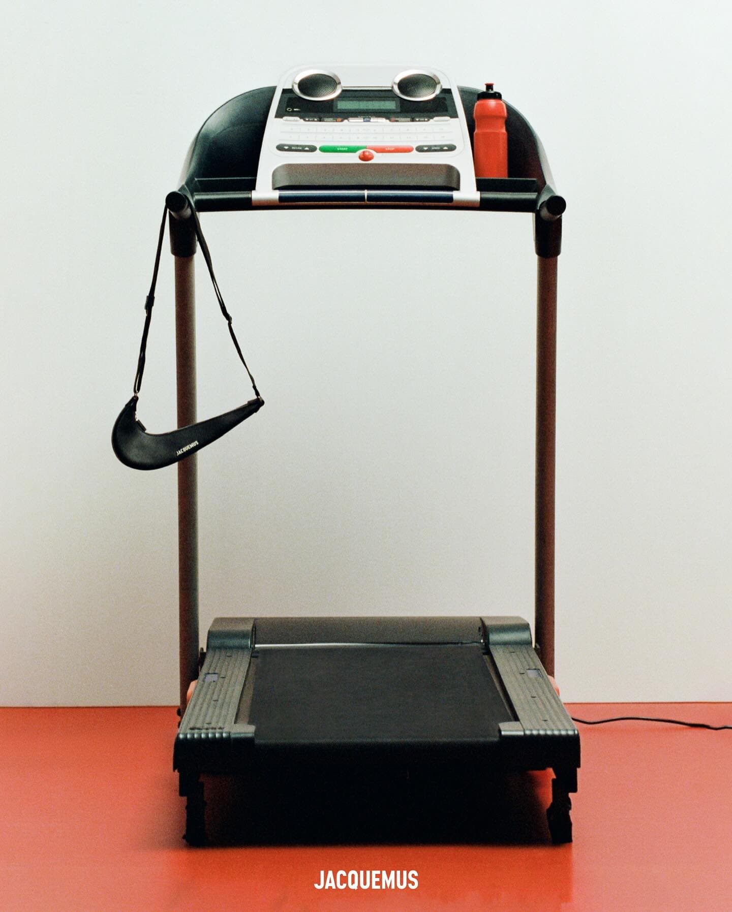 Treadmill with Nike purse, a Jacquemus collaboration, in a minimalist setting with a white wall and red floor.  Minimalist, modern.