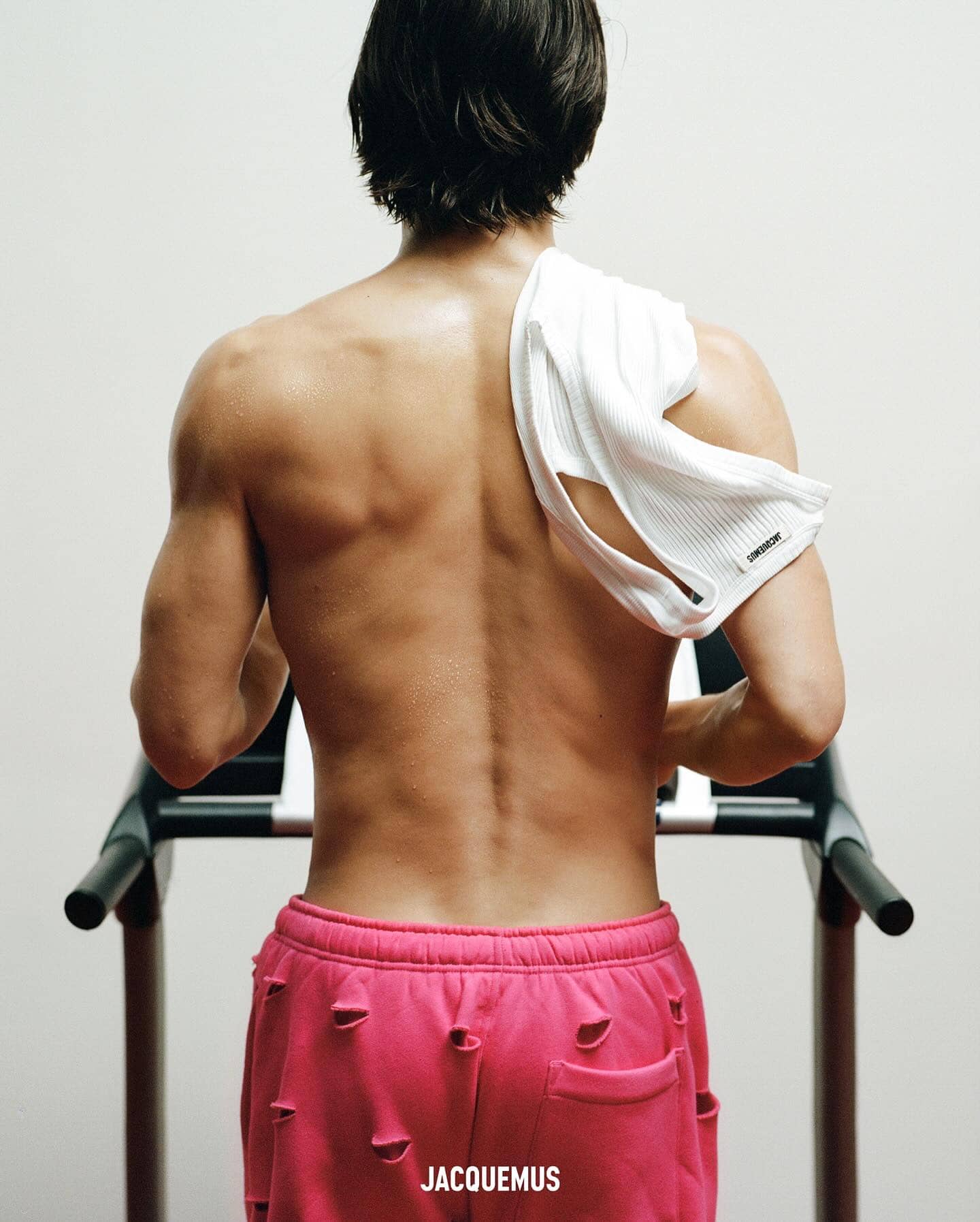 Athletic male with towel on treadmill, wearing pink shorts. Focus on back muscles and active lifestyle.
