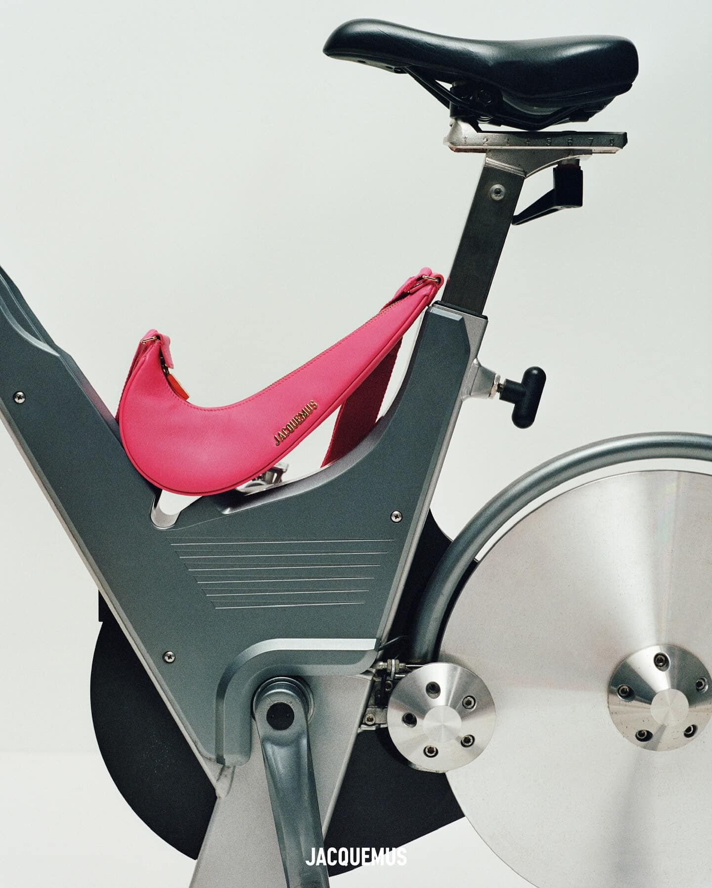 Eye-level studio shot of an indoor stationary bike with a small pink leather purse draped over the frame and seat post.