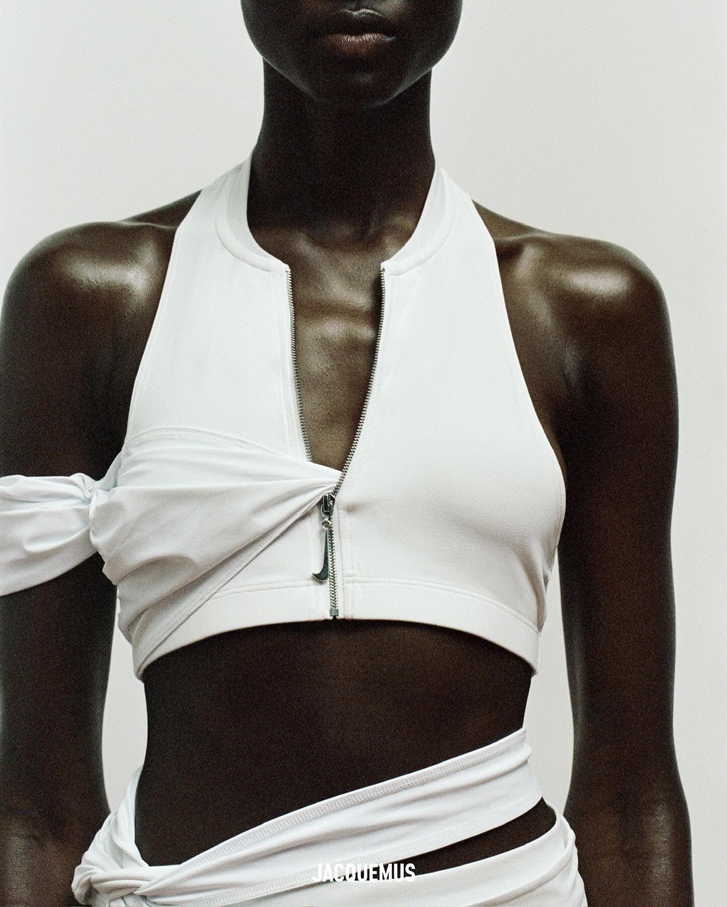Striking portrait of a Black woman in a white crop top with zipper detail and wrapped skirt, set against a clean, neutral background.