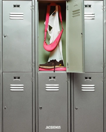 Pink bag and dark sneaker on a pink cushion inside an open grey locker, against a backdrop of adjacent lockers, well-lit.