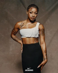 Sha’Carri Richardson in a white asymmetric crop top and black skirt against a textured backdrop for Jacquemus x Nike.