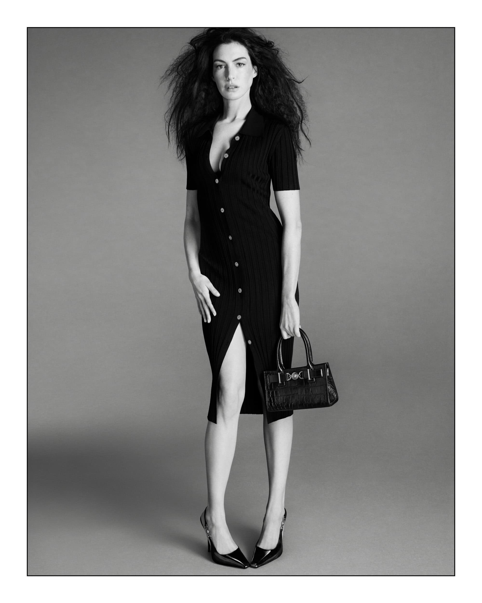 Black and white fashion shot of an adult woman in a black collared dress with a purse and high heels, posing in a studio.
